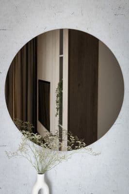 Round custom mirror with a beveled glass edge, reflecting modern interior decor and greenery, highlighting our expertise in custom glass solutions.