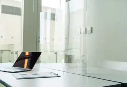Custom clear tempered glass partitions on a modern table with a laptop, showcasing versatile glass solutions for shower doors, table tops, and mirrors.