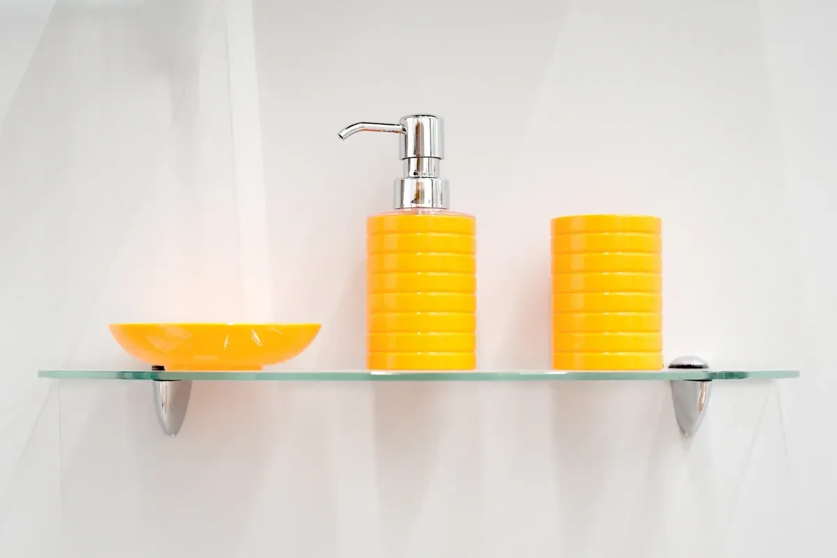 Modern glass shelf displaying yellow bathroom accessories, showcasing custom glass design and tempered glass durability.