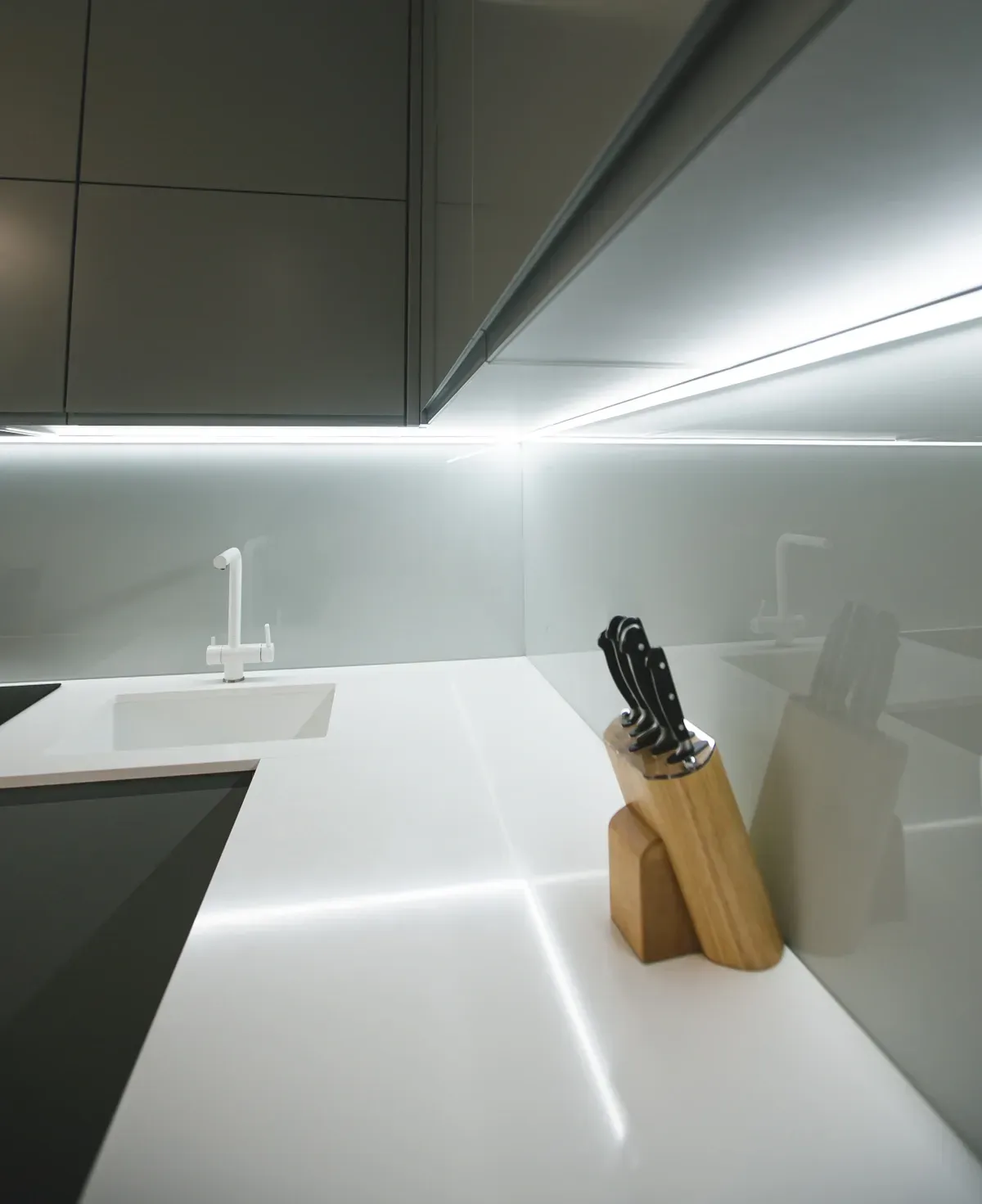 Modern kitchen with custom glass backsplash, white countertop, and knife block; showcasing sleek design for tempered and beveled glass applications.