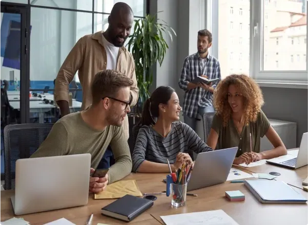 A group of professionals collaborating around a table with laptops, discussing custom glass solutions for shower doors, table tops, and mirrors, featuring tempered glass and beveled glass edge options.