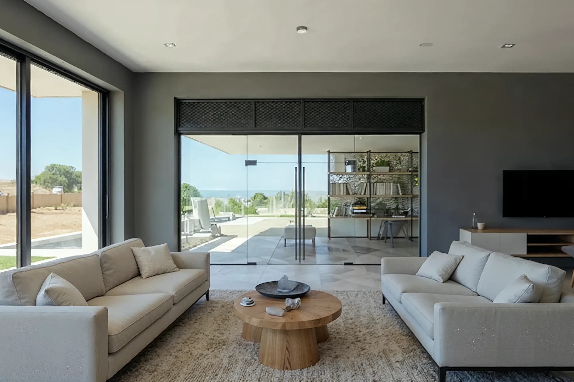 Modern living room with frameless clear glass double doors leading to a home office with a beautiful sea view.
